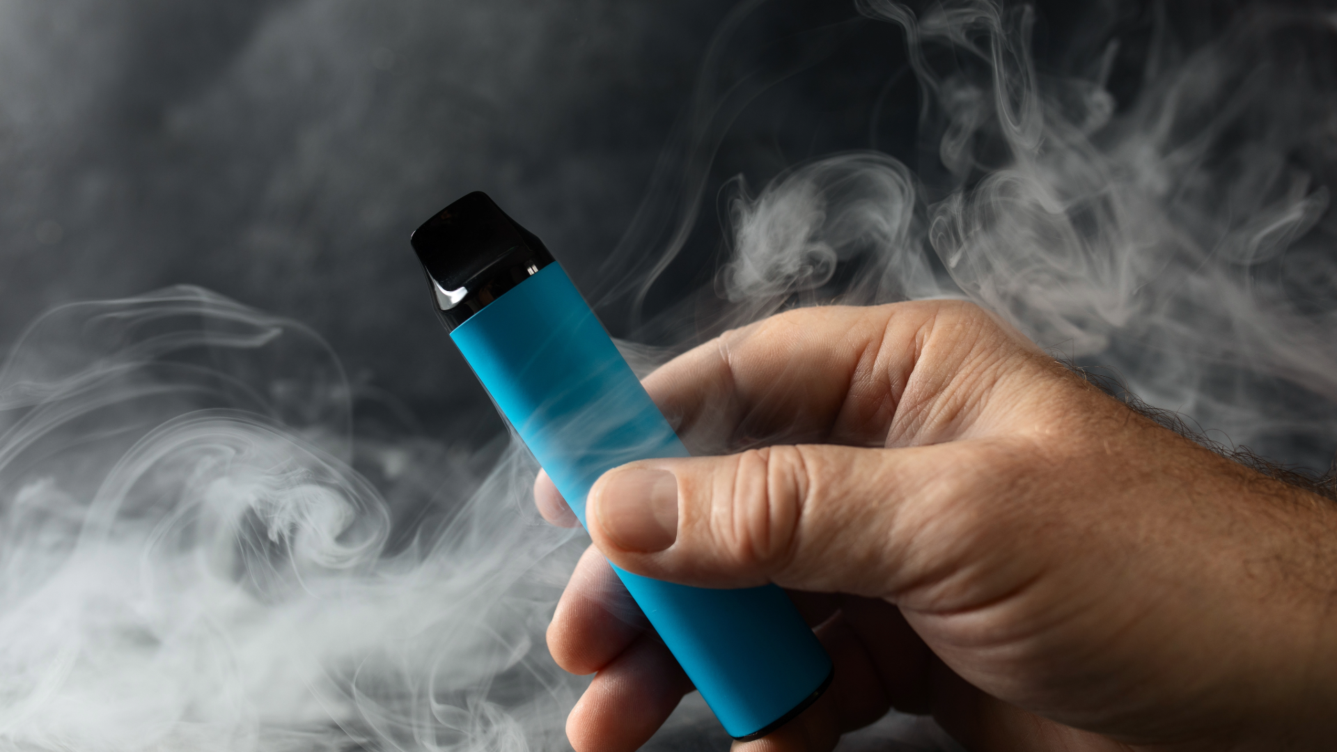 Hand holding a vape with smoke around